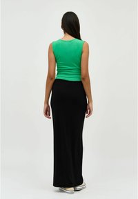 Groene mouwloze top en zwarte maxi-rok. De top is getailleerd; de rok heeft een elastische tailleband, wat zorgt voor een soepele silhoeët.