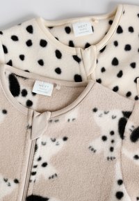 Két kisbaba szunya zsák különböző színekben: krémszínű fekete pöttyökkel és bézs barna díszítéssel, elülső cipzárral és címketagokkal.