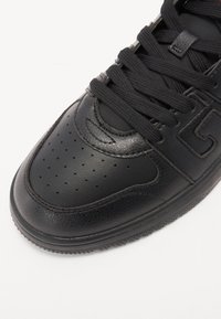 Czarne skórzane sneakersy z gładką powierzchnią, perforowanym noskiem, okrągłymi sznurowadłami oraz strukturalną podeszwą z subtelnymi detalami brandingu.