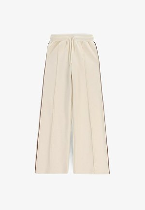 Kremowe spodnie o szerokich nogawkach z elastycznym pasem, detalem szwu z przodu, bocznymi kieszeniami oraz cienkimi ciemnymi paskami biegnącymi wzdłuż zewnętrznych szwów.
