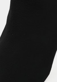 Primer plano de una tela negra texturizada con sutiles arrugas, destacando la superficie y los detalles del material.