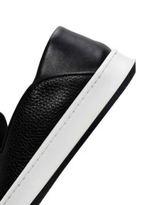 Black leather sneaker with a textured upper, smooth black heel, and a white sole. Features contrasting stitching around the midsole.