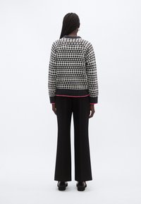 Stickad tröja med svartvit stjärnpattern, ribbade muddar och en rosa fåll, kombinerad med svarta vida byxor och svarta skor.