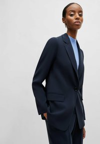 Mörkblå skräddarsydd kavaj i slät tyg, med en knappstängning, två framfickor och slagkrage.