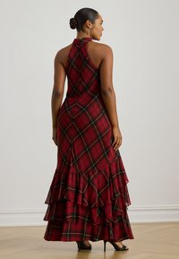 Röd rutig maxiklänning med halterneck, volanglager vid fållen och öppen ryggdesign. Materialet verkar vara lätt med en mjuk textur.
