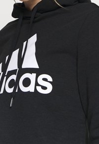 Felpa con cappuccio nera realizzata in materiale morbido, caratterizzata da un grande logo Adidas bianco sul petto, con cordini al collo.