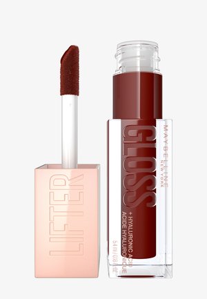 Gloss à lèvres dans un conteneur cylindrique transparent avec une base carrée en rose doré. Dispose d'un applicateur en forme de pied de chevreuil incliné, d'une couleur rouge profond et d'un texte en relief.