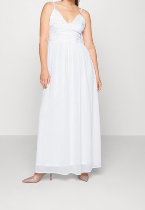 Robe longue blanche avec un corsage en dentelle, des bretelles spaghetti ajustables et une jupe fluide. Associée à des talons hauts nus étincelants.