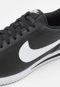 Adidași negri din piele cu logo alb Nike, design cu șireturi, suprafață texturată și model de talpă în zig-zag. Vedere de sus care evidențiază caracteristicile cheie.