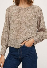 Langærmet bluse i let, mønstret stof med en beige baggrund og olivenfarvede pletter. Rund halsudskæring og let cropped design.