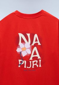 Κόκκινο βαμβακερό T-shirt με έντονο λευκό και μπλε κείμενο, και γραφικό με ροζ λουλούδι, με στρογγυλή λαιμόκοψη και λεία υφή.