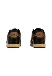 Chaussures de sport marron et beige avec un dessus en cuir lisse, un col rembourré et une semelle en caoutchouc, présentant le logo "Redskins" au niveau du talon.