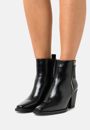 Bottines en cuir noir avec bouts pointus, fermeture éclair latérale et talons blocs. Texture lisse et design épuré.