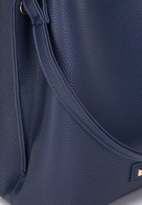 Mörkblå läderhandväska med en texturerad yta, med en böjd design och detaljer i guldton. Slät, strukturerad form.