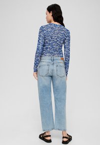 Langdurige mouwloze blauwe patroon top in een transparante stof, gecombineerd met lichtblauwe wijde denim jeans. Zwarte sandaaltjes met bandjes maken de outfit compleet.