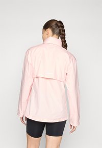 Light pink waterproof jacket with long sleeves, high collar, and a back vent. Features a reflective strip near the hem. Breathable fabric.