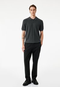 Donkergrijze korte mouw polo met een ribbelstructuur en een twee-knopen knoopsluiting, gecombineerd met zwarte op maat gemaakte broeken en zwarte schoenen.