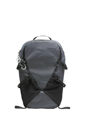 Zaino in poliestere grigio con accenti neri. Presenta molteplici cinghie regolabili e cerniere, texture liscia e un logo centrale. Design compatto.