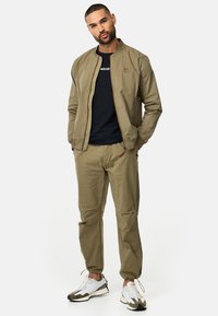 Oliwkowa bomberka z zamkiem, w zestawie z dopasowanymi spodniami tapered. Czarno t-shirt pod spodem oraz białe sneakersy z szarymi akcentami.