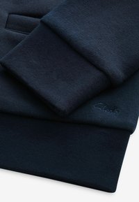 Sweat-shirt bleu marine plié montrant des poignets côtelés et un logo brodé subtil sur le tissu.