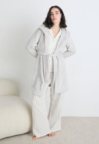 Halat de baie gri matlasat cu glugă și curea, suprapus peste un top de pijama alb și albastru cu dungi și pantaloni evazați, pe un fundal deschis.