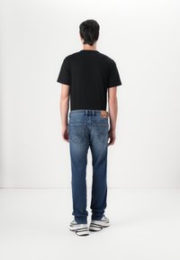 Blauwe denim jeans met een rechte snit, met een vervaagde textuur en twee achterzakken. Gecombineerd met een plain zwarte T-shirt met korte mouwen en sneakers.