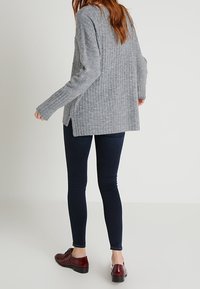 Grå, ribbad tröja med långa ärmar, sidsprund och avslappnad passform. Matcher med mörka skinny jeans och vinröda snörskor.