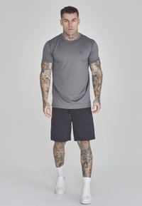 Tricou gri cu mânecă scurtă, cu un design ajustat și un logo mic. Asortat cu pantaloni scurți negri cu buzunare și pantofi sport albi.