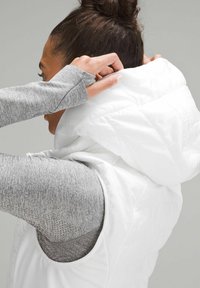 Gilet bianco imbottito con cappuccio viene regolato; presenta un design trapuntato e una maglietta a maniche lunghe grigia morbida sotto.
