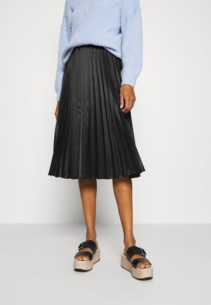 Schwarzer, plissierter Midirock mit glatter Textur, kombiniert mit schwarzen Plateau-Sandalen mit Schnalle und beiger Sohle. Das Oberteil ist ein hellblauer Pullover.