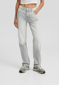 Jeans de denim gris claro con un corte recto, cinco bolsillos y un desvanecimiento sutil. Combinados con zapatillas grises y blancas.