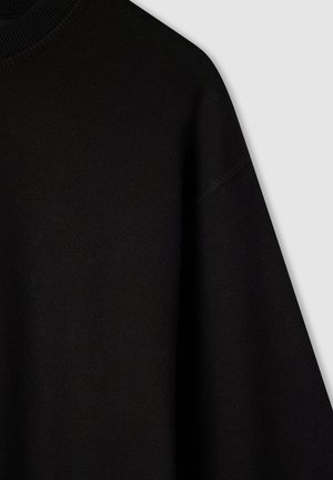 Czarna bluza z dekoltem okrągłym, o miękkiej teksturze i luźnym kroju. Widoczne szwy wzdłuż rękawów i dekoltu podkreślają strukturę.