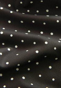 Tissu noir à texture lisse avec des petits pois blancs espacés uniformément et des plis doux créant des ombres délicates.