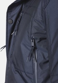 Marineblaue Jacke aus strukturiertem Stoff mit Reißverschlüssen, Kordelzügen und einer Tasche auf der Vorderseite für Funktionalität und Stauraum.