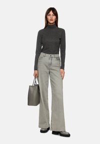 Grauer Rollkragenpullover, hellgraue weiter Jeans mit Nietenakzenten, schwarze Plattformstiefel und eine graue Handtasche. Glatter Stoff und strukturierte Form.