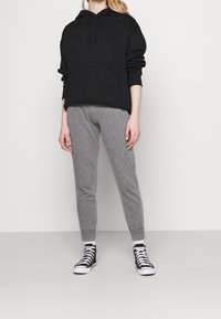 Svart munkjacka med känguruficka, tillsammans med ljusgrå tapered sweatpants. Svartvita högklackade sneakers fulländar outfiten.