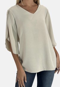 Lysebeige V-hals bluse med korte, løstsiddende ærmer, lavet af et blødt, tekstureret stof. Skræddersyet pasform, rundet kant og ingen synlige detaljer.