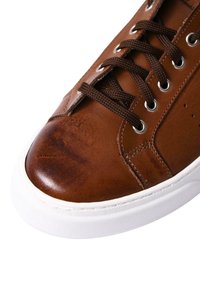 Sneaker in pelle marrone con finitura liscia, suola in gomma bianca e lacci marroni infilati attraverso occhielli in argento.