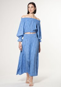 Blauw off-shoulder top met elastische plooien bij de halslijn en geborduurde bloemen, gecombineerd met een bijpassende lange rok, beide van lichtgewicht stof.