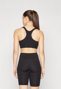 Μαύρο σπορ σουτιέν με σχέδιο racerback και αντίστοιχα ψηλόμεσα σορτς, και τα δύο φτιαγμένα από απαλό, ελαστικό ύφασμα.