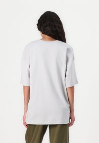 T-shirt oversize gris clair, manches courtes, en coton doux. Encolure ronde simple, ourlet droit, sans motifs ni accents visibles.