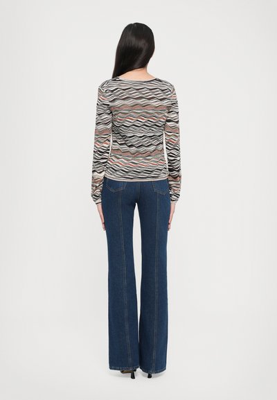 Maglietta a maniche lunghe con motivo ondulato multicolore realizzata in materiale leggero, abbinata a jeans a zampa d'elefante blu scuro con dettagli delle cuciture in evidenza.