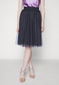 Gonna in tulle nero con vita arricciata, design a strati e pois metallici sparsi, abbinata a sandali con cinturini decorati.