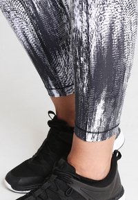 Černobílé legíny s vzorovaným designem, s texturovaným vzorem, přiléhavým střihem a kotníkovou délkou, spárované s černými sportovními botami.