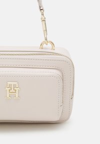 Bolso de piel rosa claro con herrajes dorados, que cuenta con un compartimento principal con cremallera y un pequeño bolsillo frontal con cremallera. Logo grabado en la parte frontal.