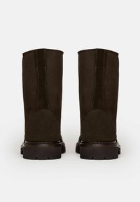 Botas de ante marrón oscuro con un upper liso, refuerzo en la parte trasera y suela de goma texturizada con patrones de dibujo profundo.