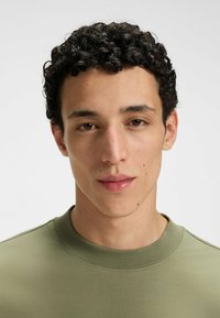 Knit olive-green t-shirt with a crew neck, featuring a smooth texture and subtle stitching details around the neckline and shoulder.