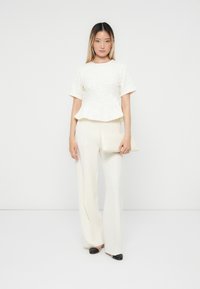 Bijela teksturirana peplum bluzica uparena s krojenim bijelim hlačama. Outfit upotpunjuje elegantna bijela torbica i cipele u dvije boje.