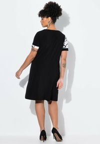 Robe noire à manches courtes ornée d'accents en motifs blancs ; tissu lisse, coupe mi-longue et fentes latérales discrètes pour faciliter les mouvements.