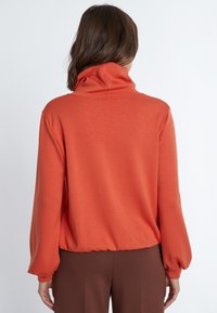 Oranger Pullover mit hohem Kragen, lockerer Passform und langen Ballonärmeln. Verfügt über einen gerafften Saum und eine glatte Textur.